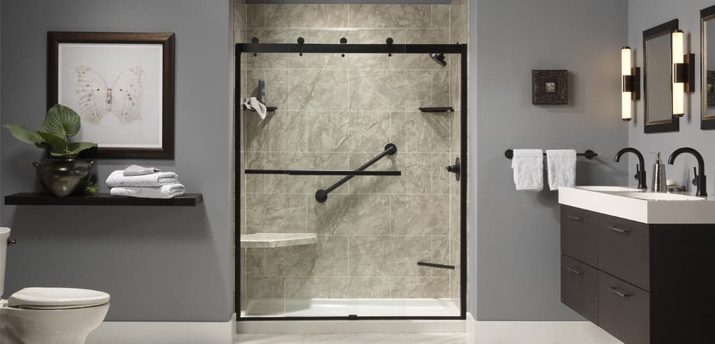 A walk-in shower with a black-framed glass screen, a horizontal grab bar, and grey marble-look wall tiles