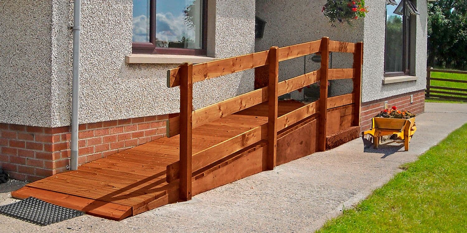 A permanent timber ramp with a timber handrail running up to the door of a rendered stone house