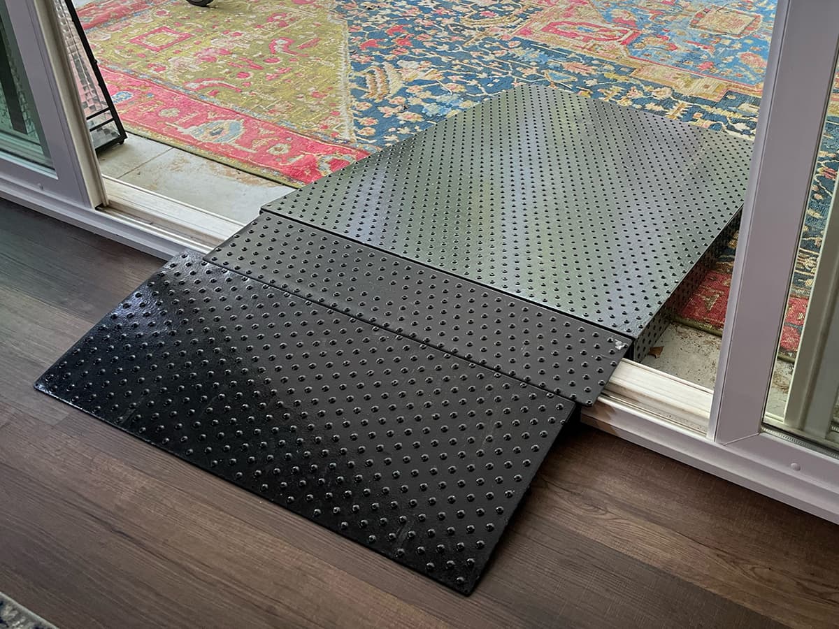 A black rubber threshold ramp with a studded surface bridging a sliding glass door onto a timber floor