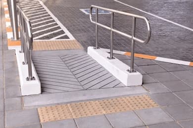 A concrete access ramp with steel handrails on both sides and yellow tactile paving at the top and bottom