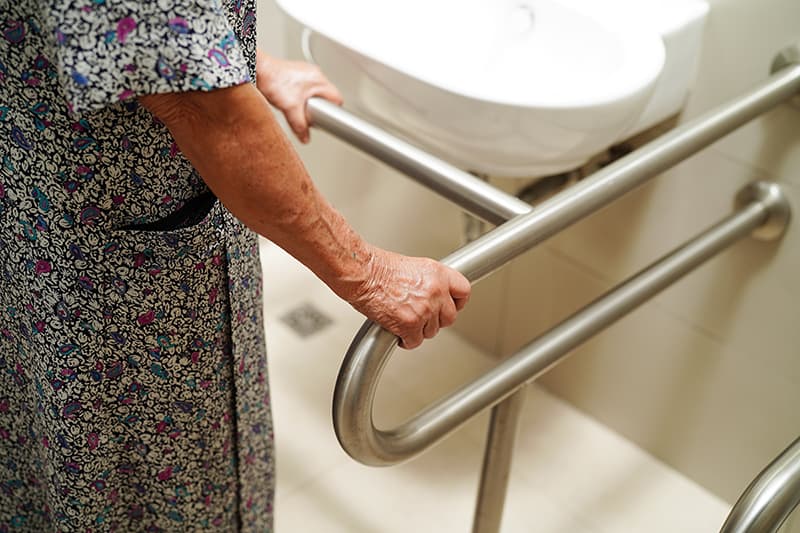The hands of an older woman gripping a curved stainless steel rail fixed beneath a basin