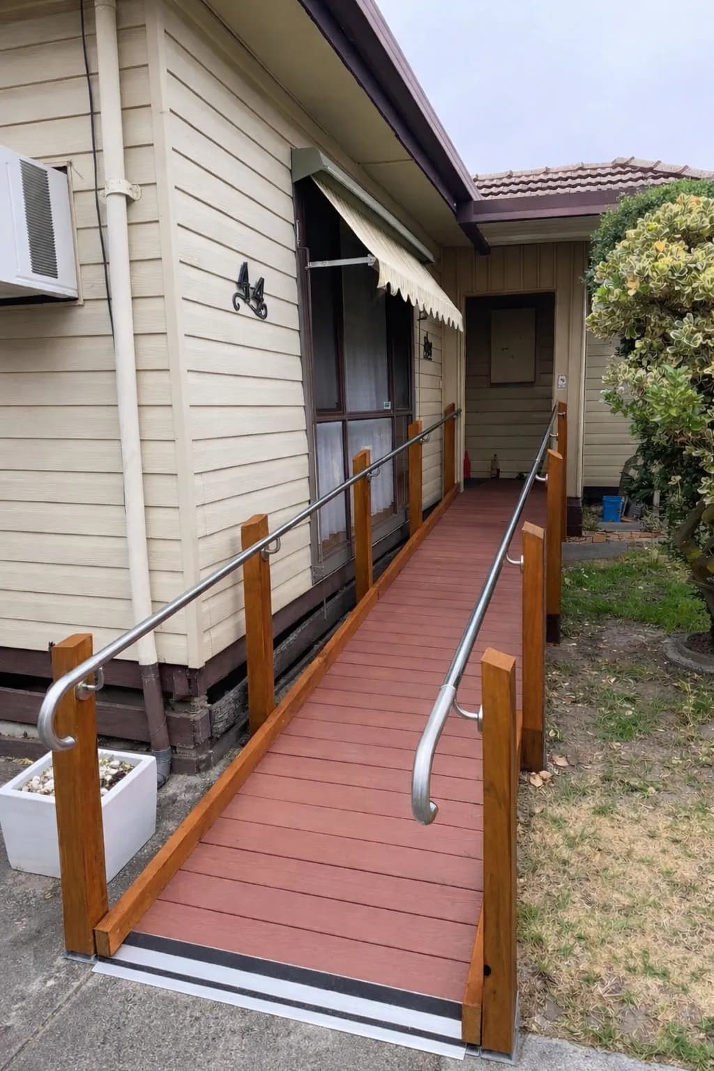 A timber-framed access ramp with composite decking and steel handrails running along the side of a weatherboard home