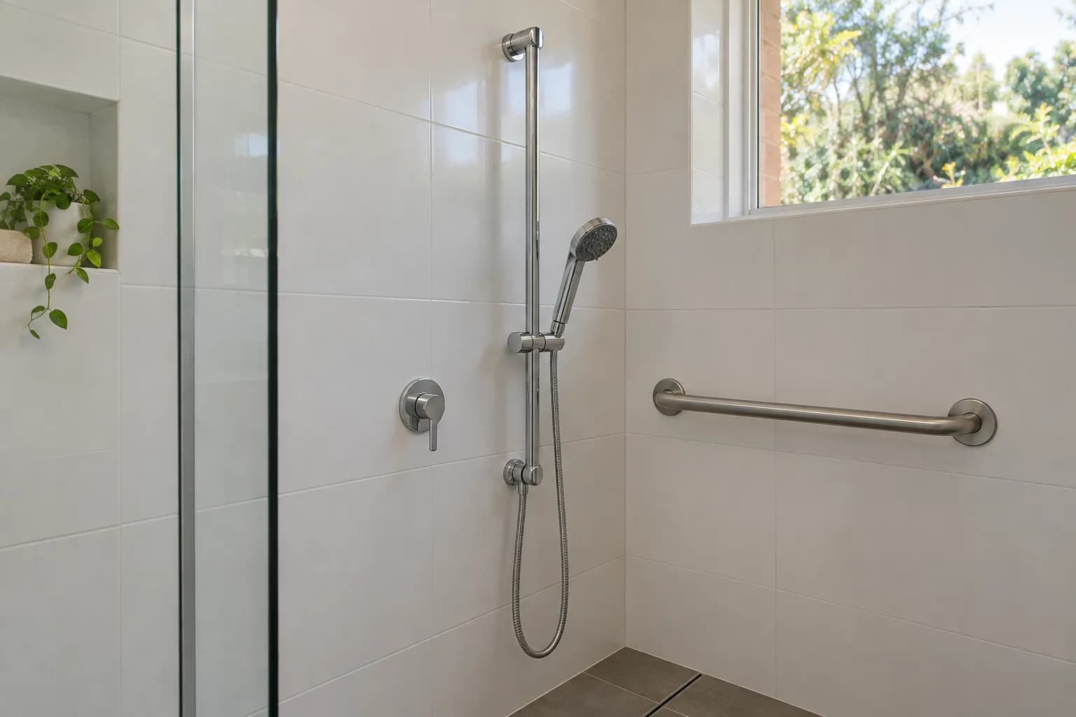 A chrome handheld shower on a sliding bracket on a vertical rail, next to a lever mixer with a grab rail nearby