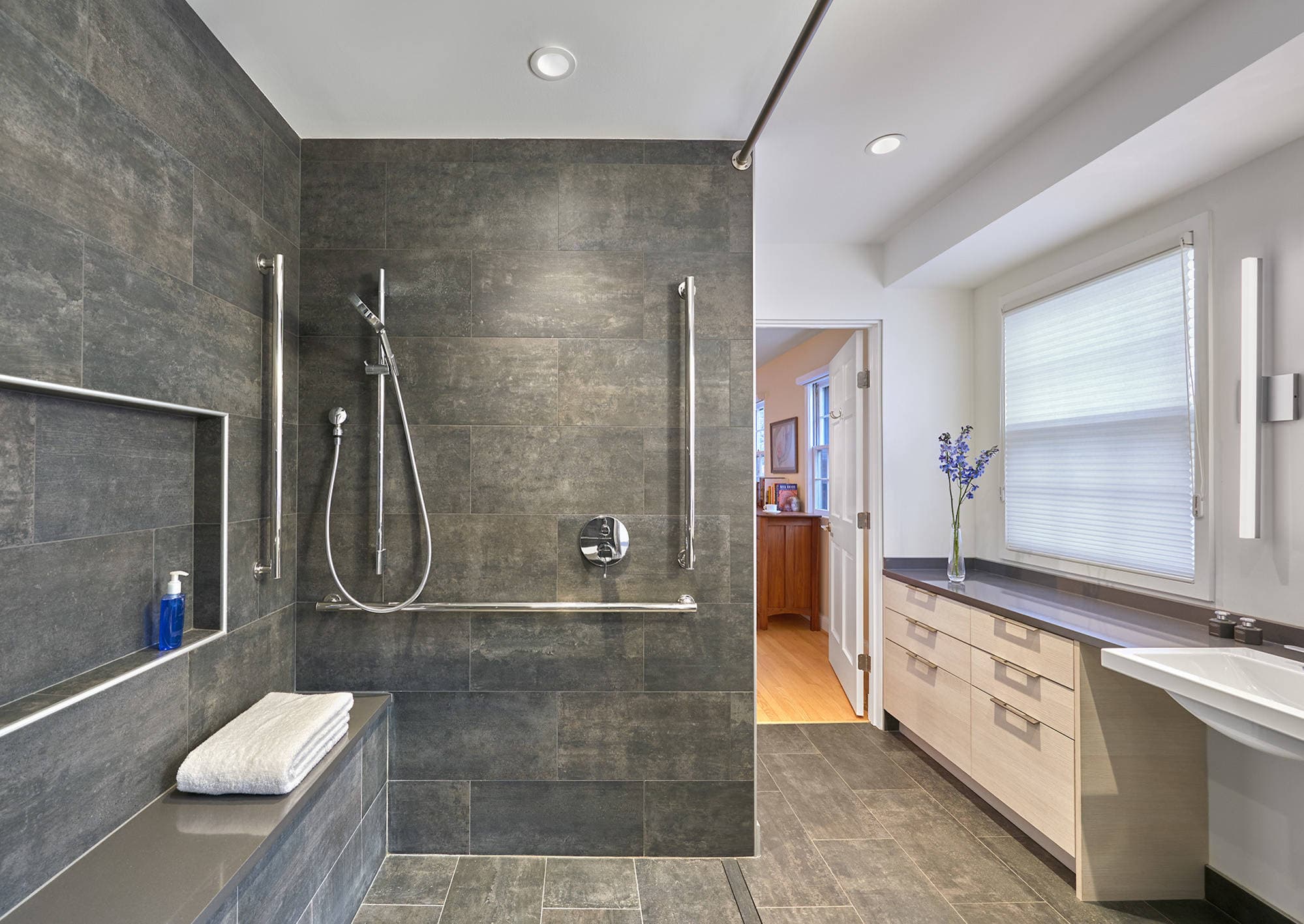 A modern walk-in shower with a built-in bench, grab rails, and textured grey tiles