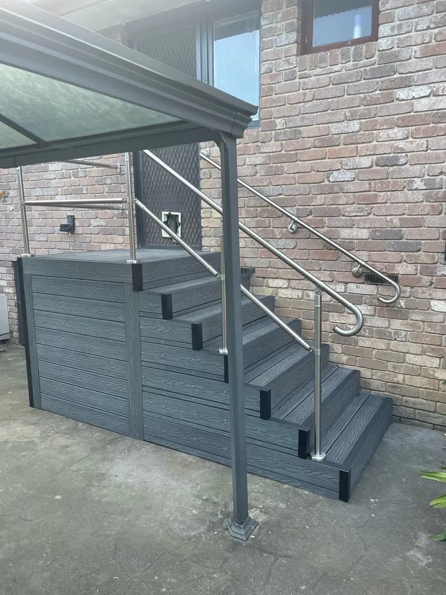 A flight of grey composite steps with contrast nosings and a stainless handrail, built against a brick wall