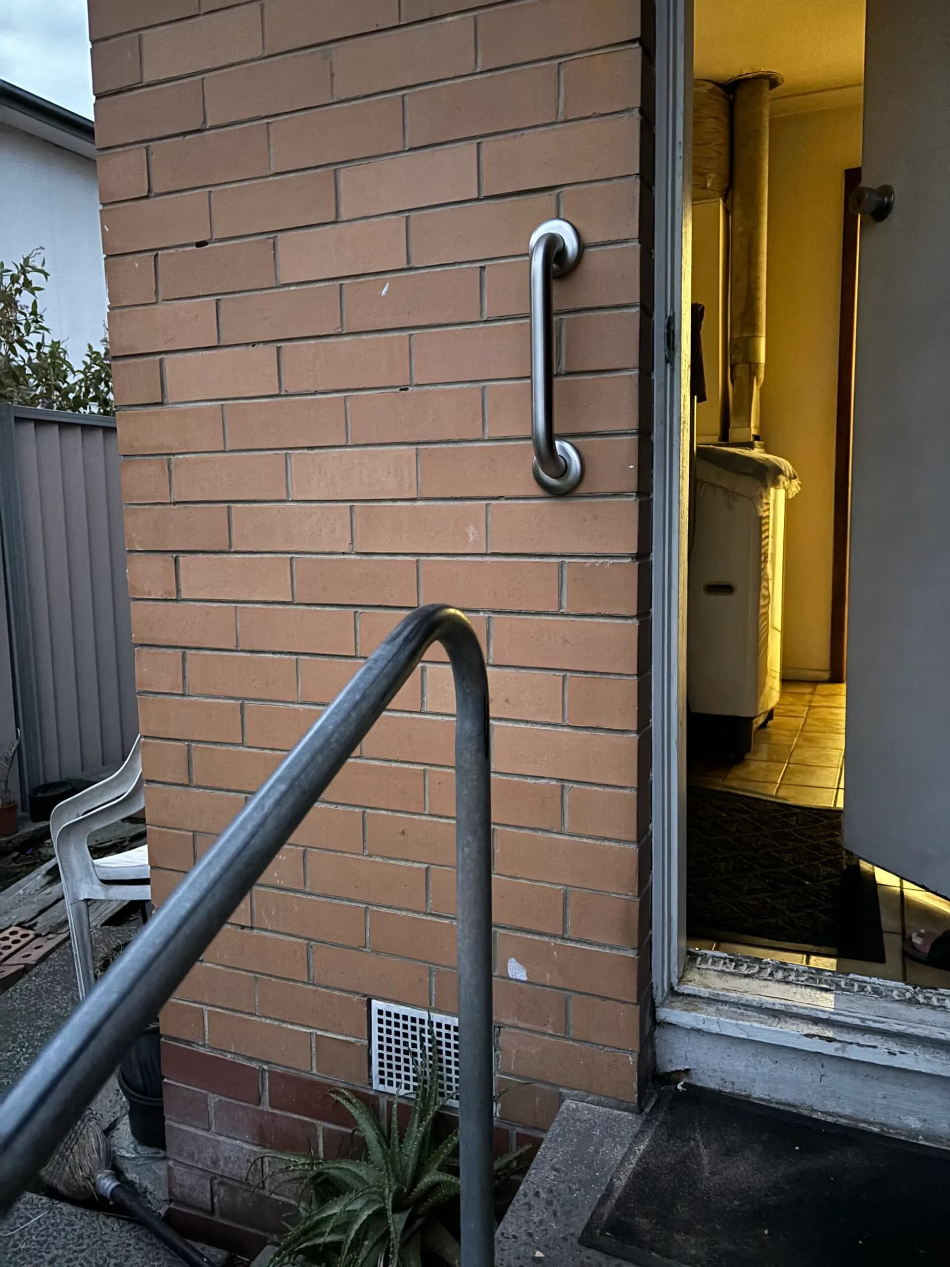A stainless steel handrail running along a brick wall and down to a paved path beside a side entrance