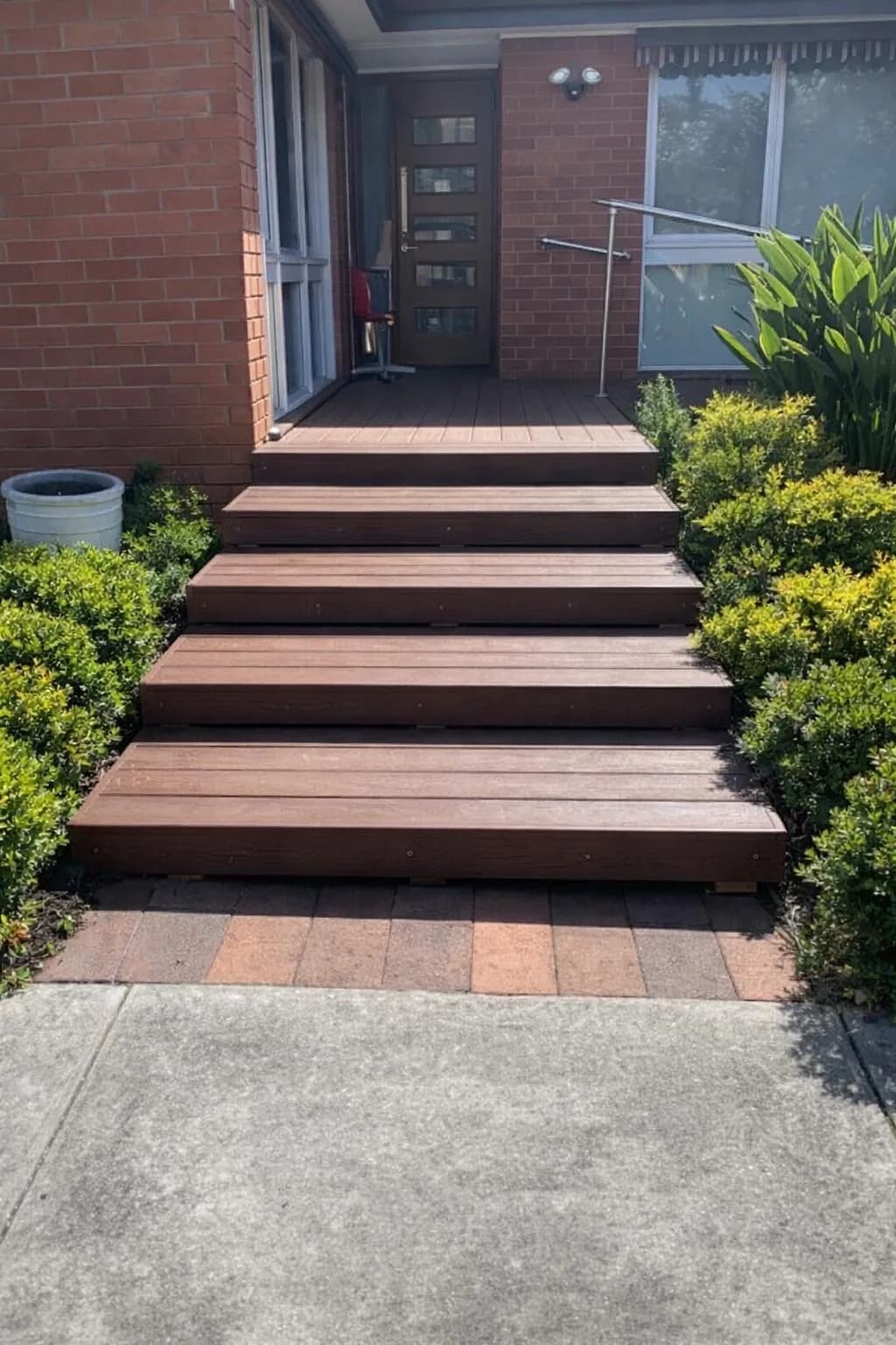 Timber entry steps with a stainless steel handrail alongside, leading up to a house door