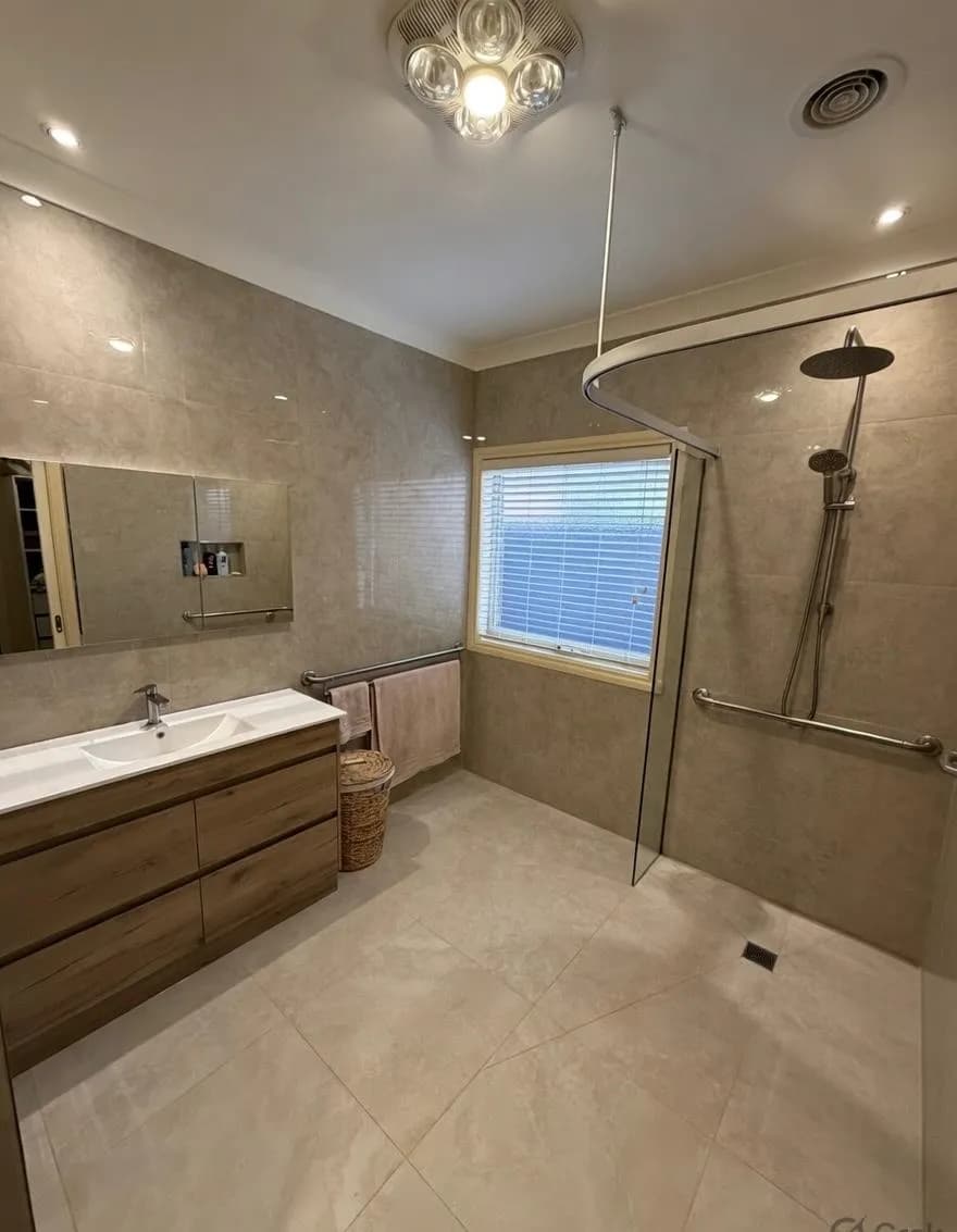 A completed bathroom with a timber vanity, large mirror, and a curved shower rail beside the shower recess