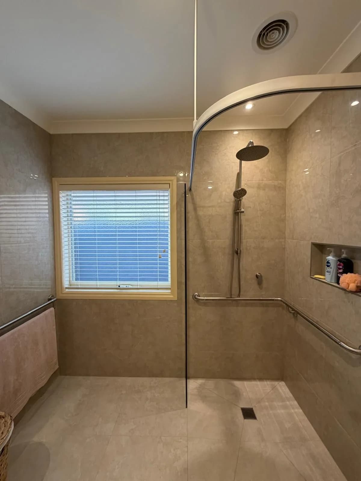 A tiled bathroom with a level-access shower, wall-mounted grab rail, and recessed shelf