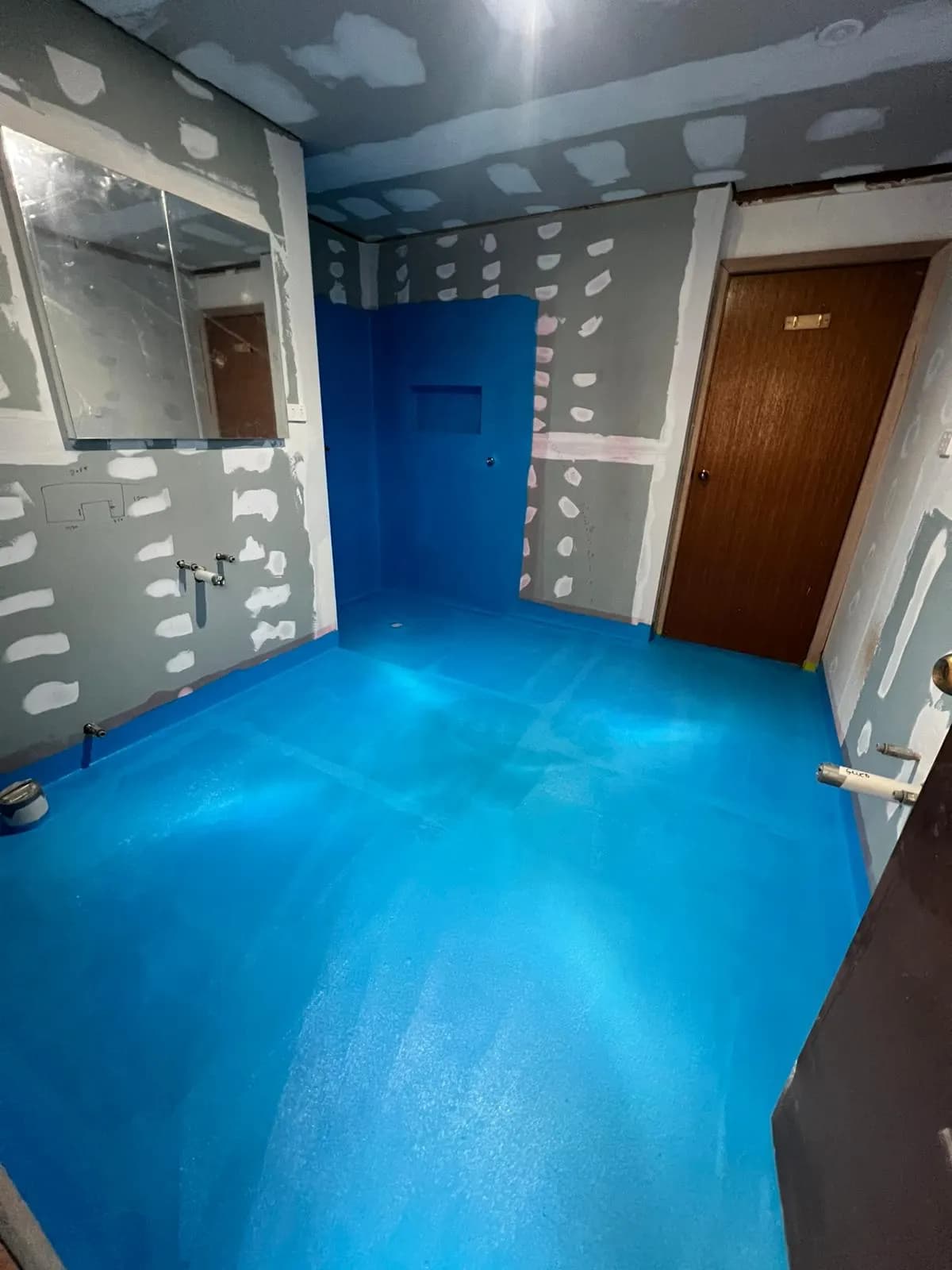 A stripped-back bathroom with blue waterproofing membrane across the floor and shower wall, ready for tiling
