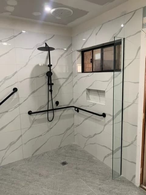 A marble-tiled shower with black grab rails on the wall