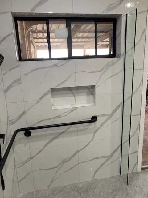 A tiled shower niche with an angled grab rail mounted on the wall beside it