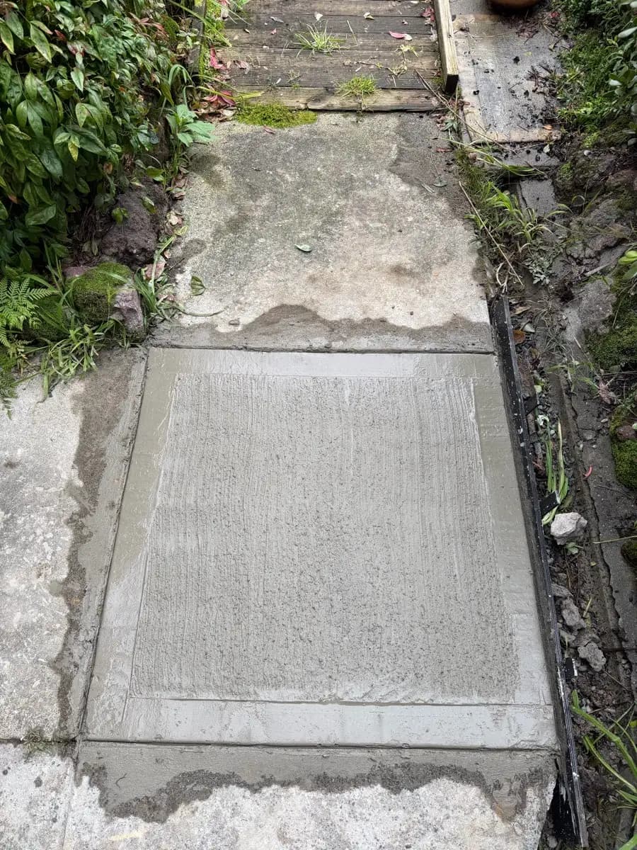 A new concrete slab poured up against an older path, filling a broken section beside a garden bed