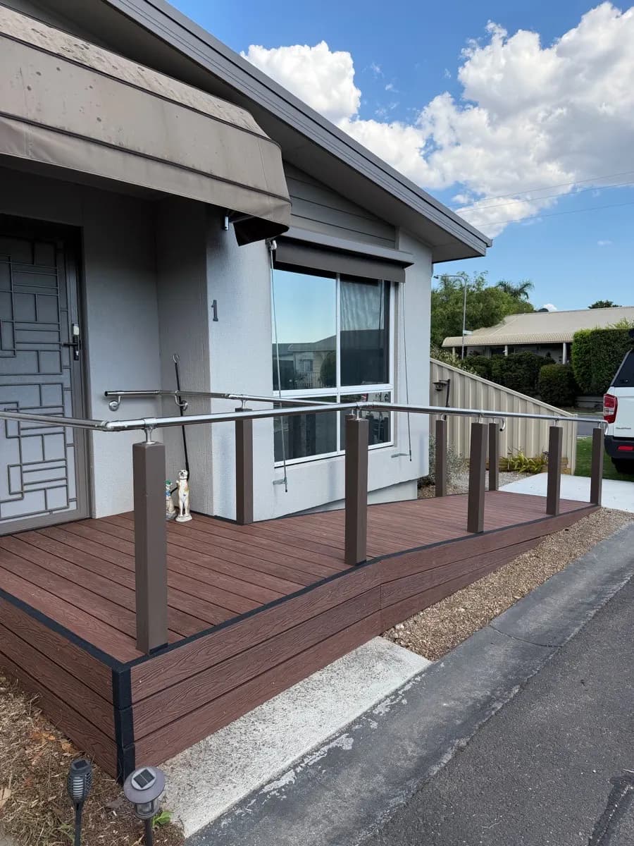 A red-brown composite deck at the front door of a house, with dark posts and a stainless steel handrail