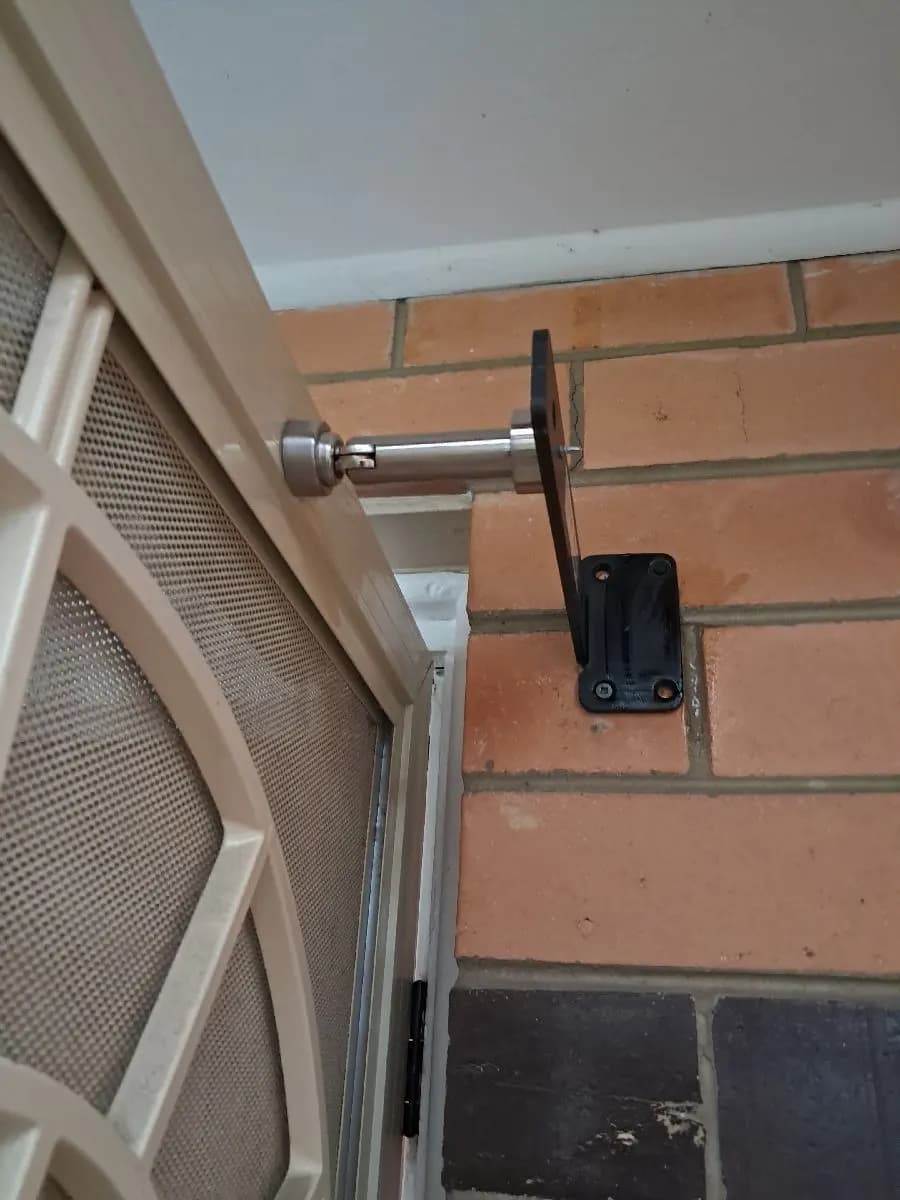 A stainless magnetic catch on a brick wall holding a screen door fully open, clear of the doorway