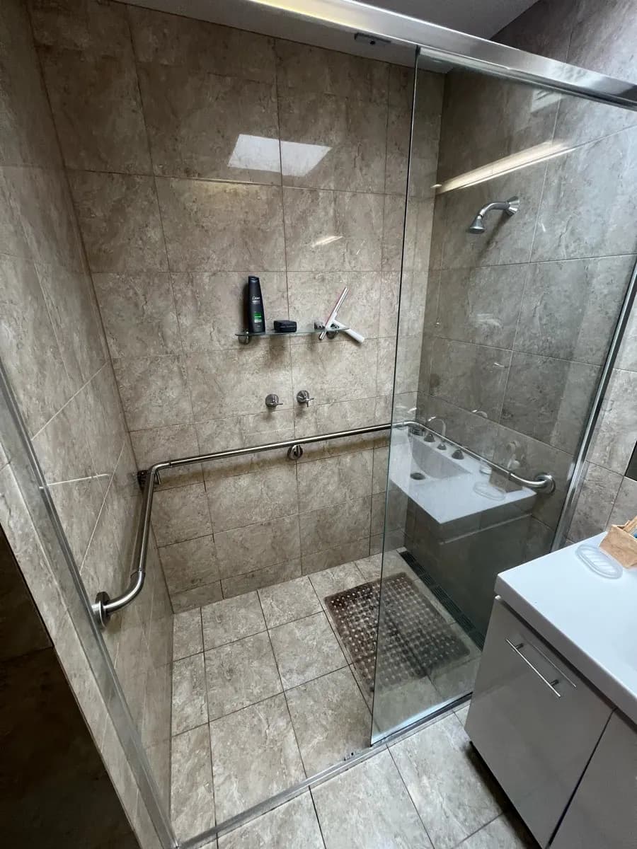 A large tiled shower recess with an angled stainless grab rail across two walls and a tiled floor waste