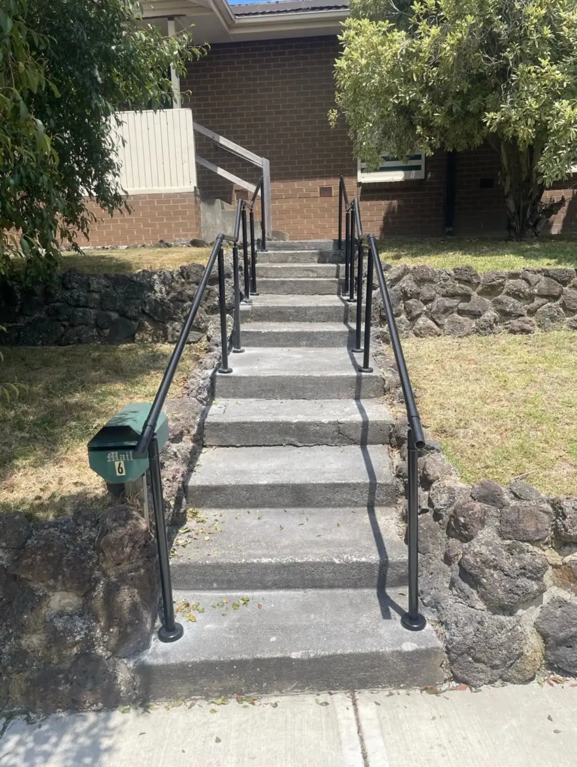 Matte black banister rails on both sides of a long flight of concrete steps leading up to a brick house