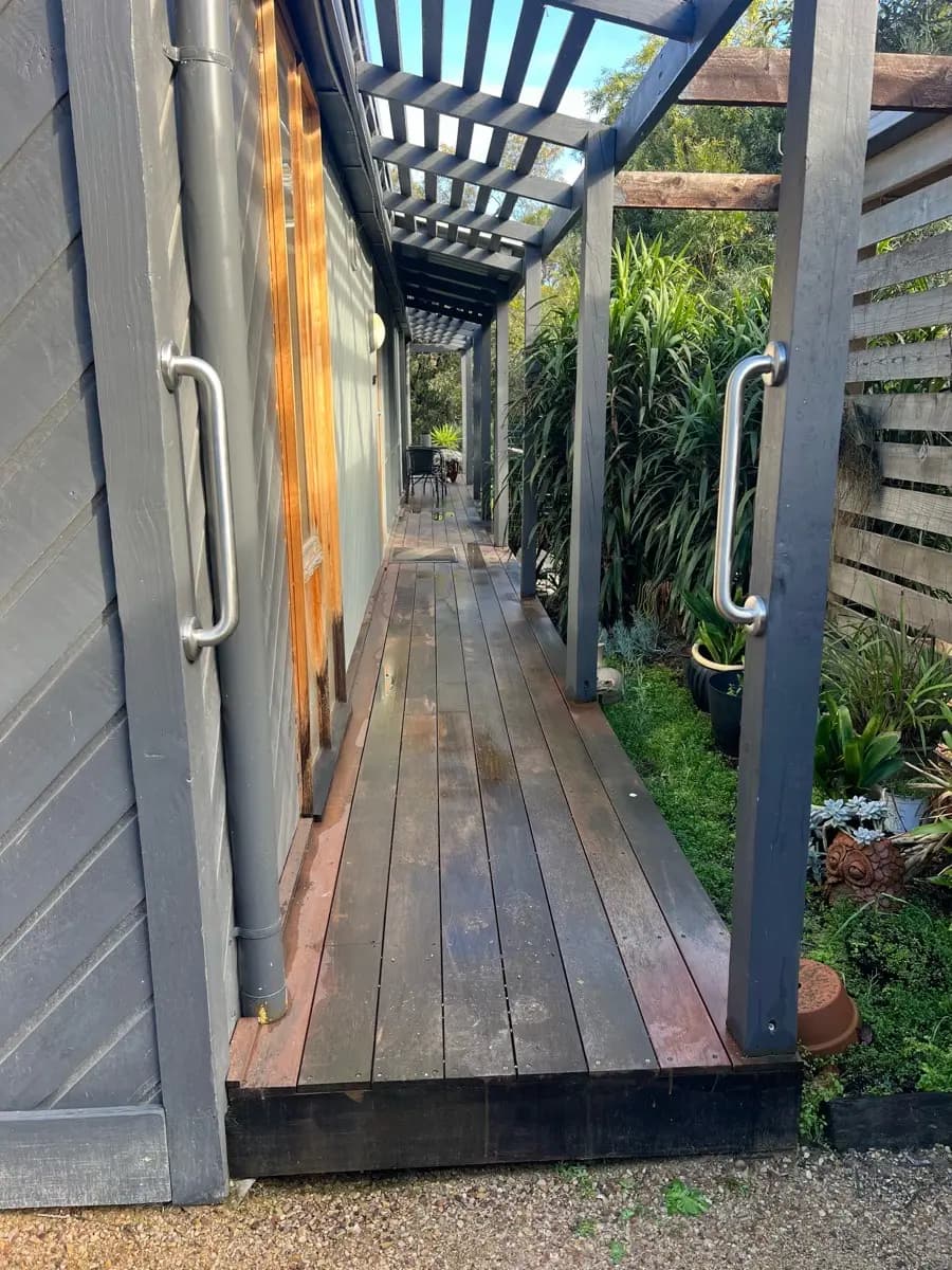 Two stainless grab rails fixed either side of a timber deck walkway between a house wall and a garden