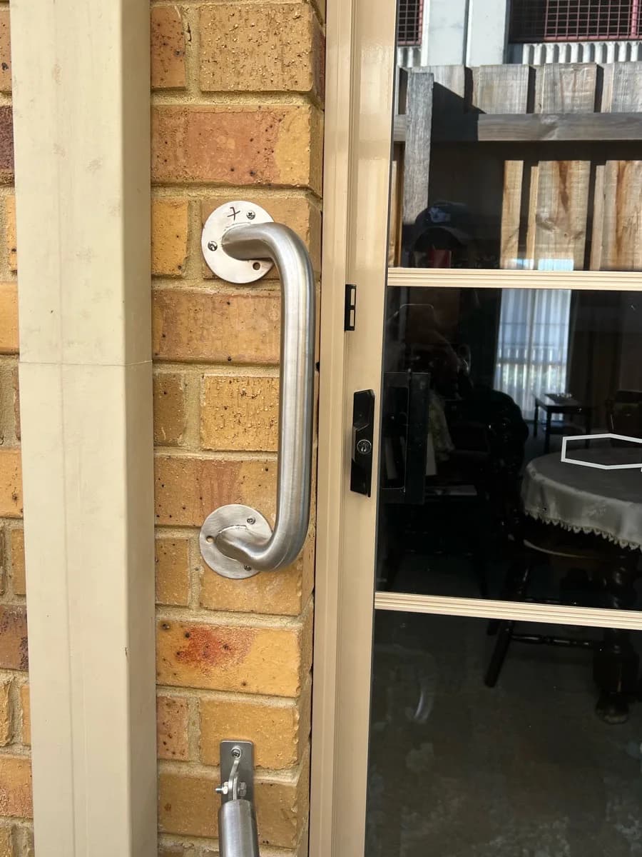 A stainless steel grab rail fixed upright to a brick wall beside a sliding glass door