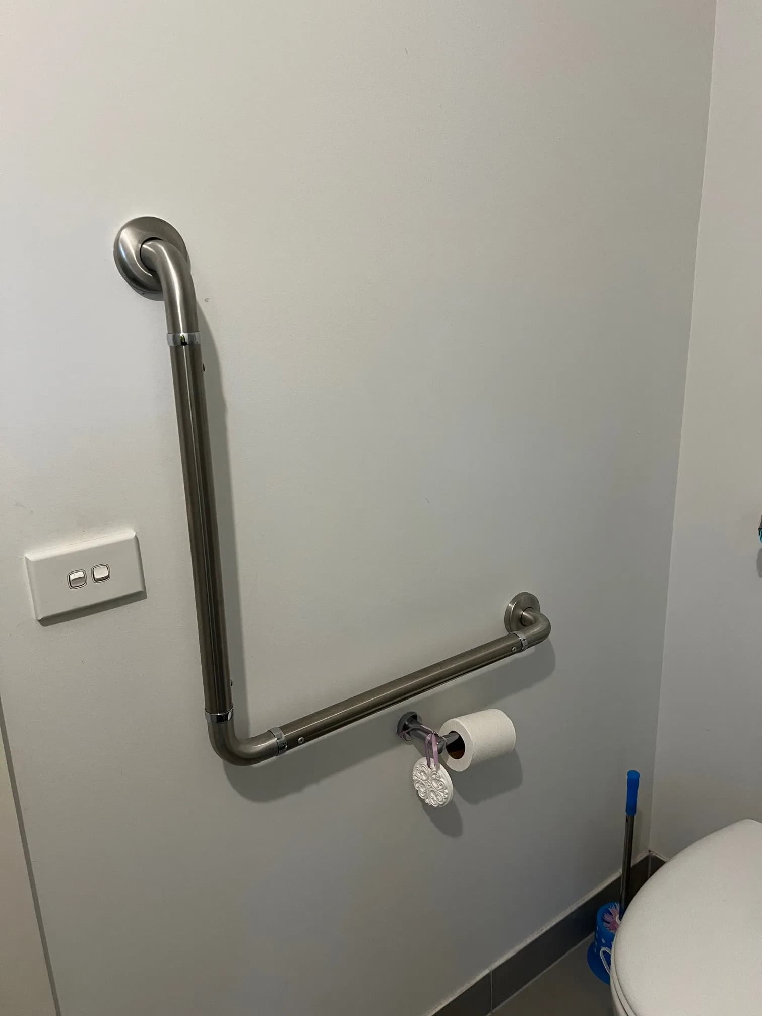 A stainless steel angled grab rail installed on the wall beside a toilet