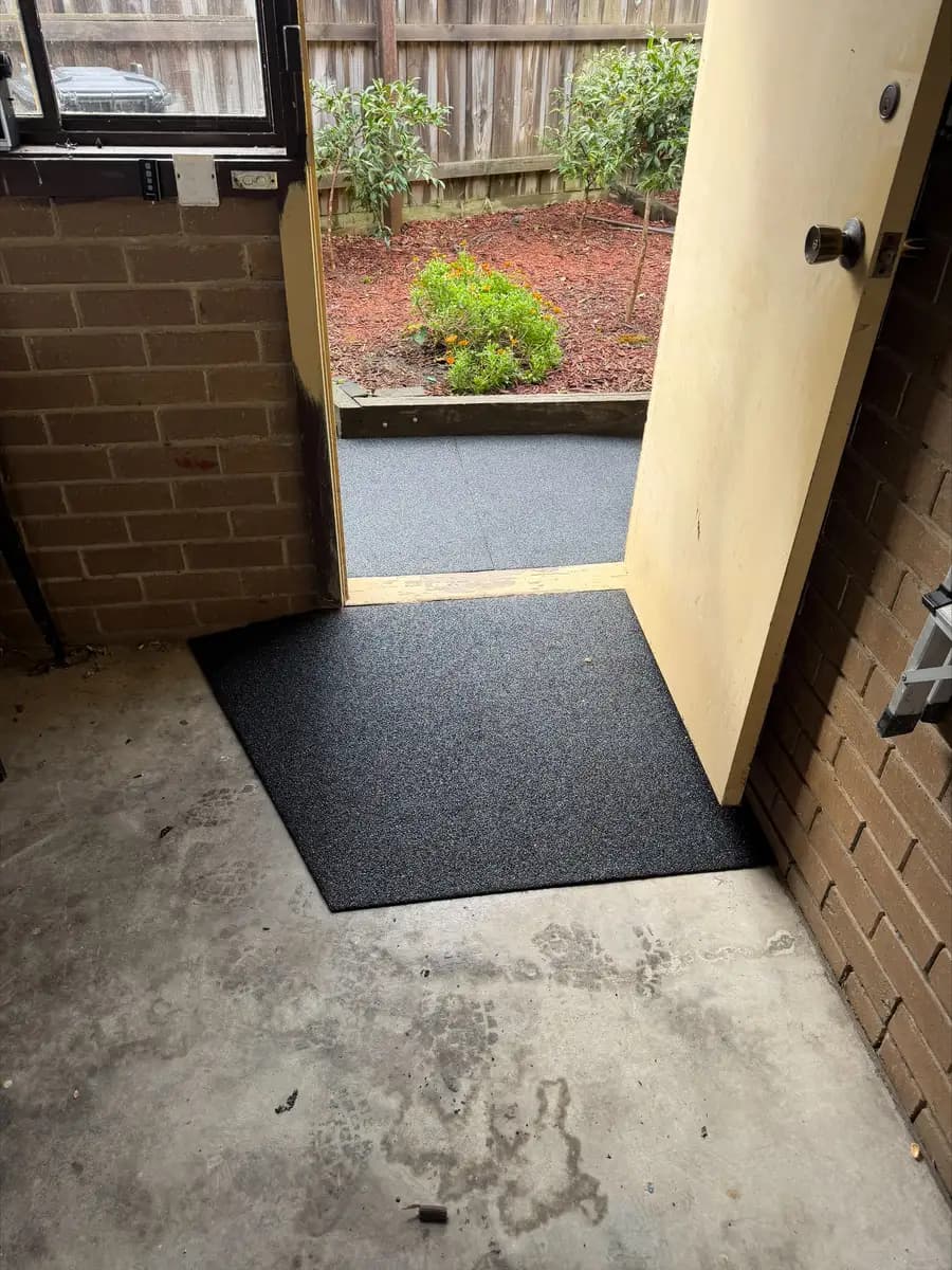 A black rubber ramp laid inside a doorway, bridging the step down to a concrete porch