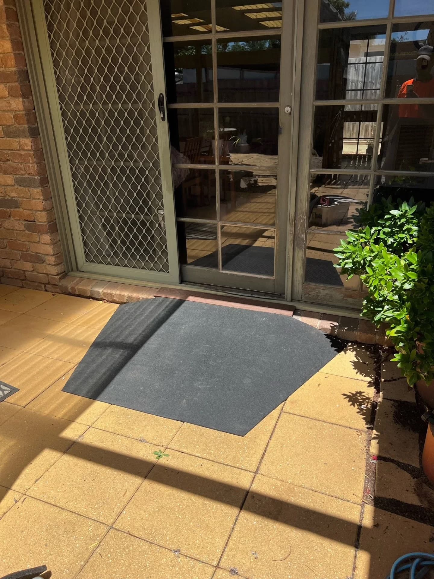 A black rubber threshold ramp laid at a sliding door, levelling the step between the room and a paved courtyard