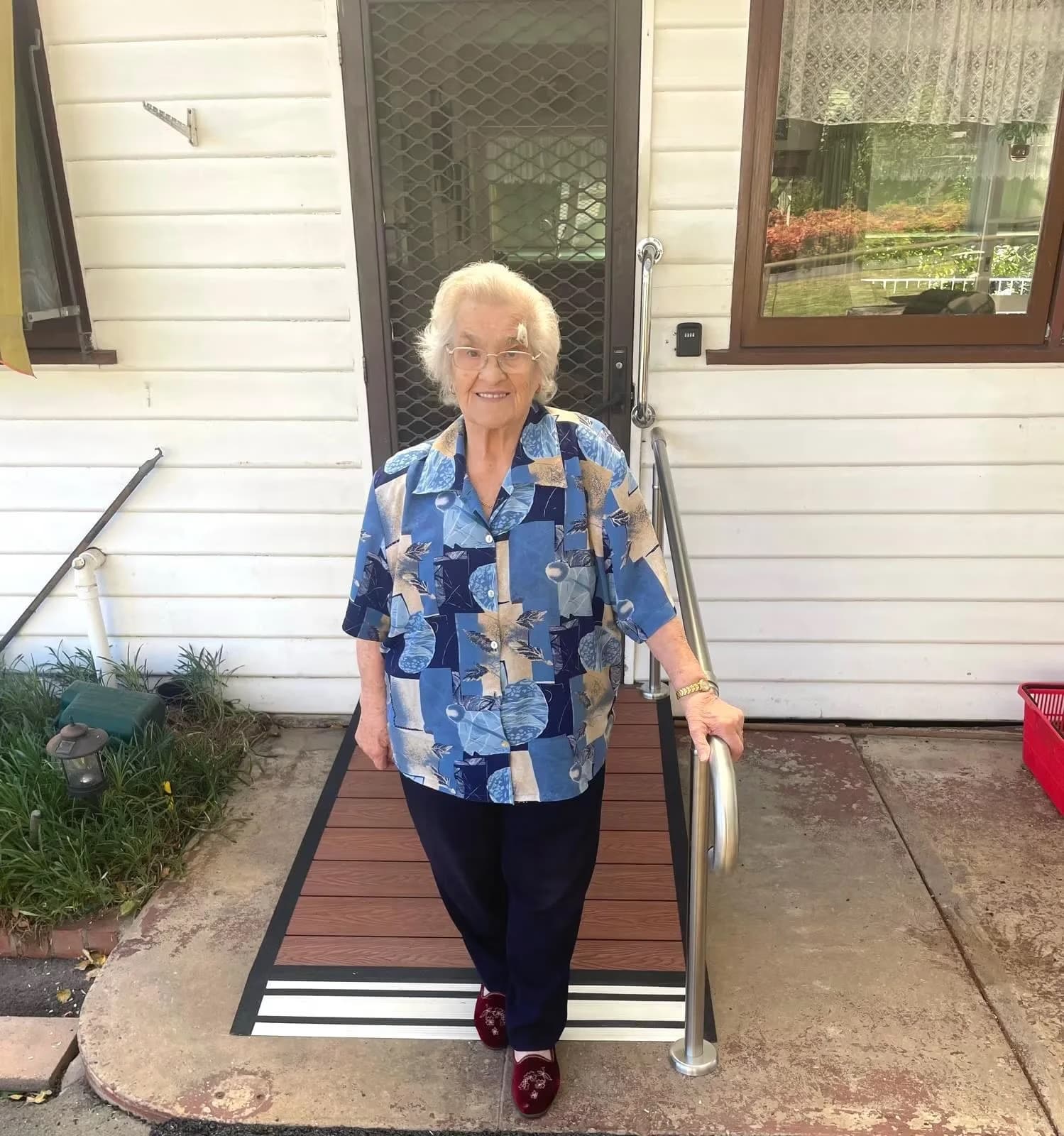 An older woman steadying herself on the handrail as she walks down a newly built access ramp at her front door