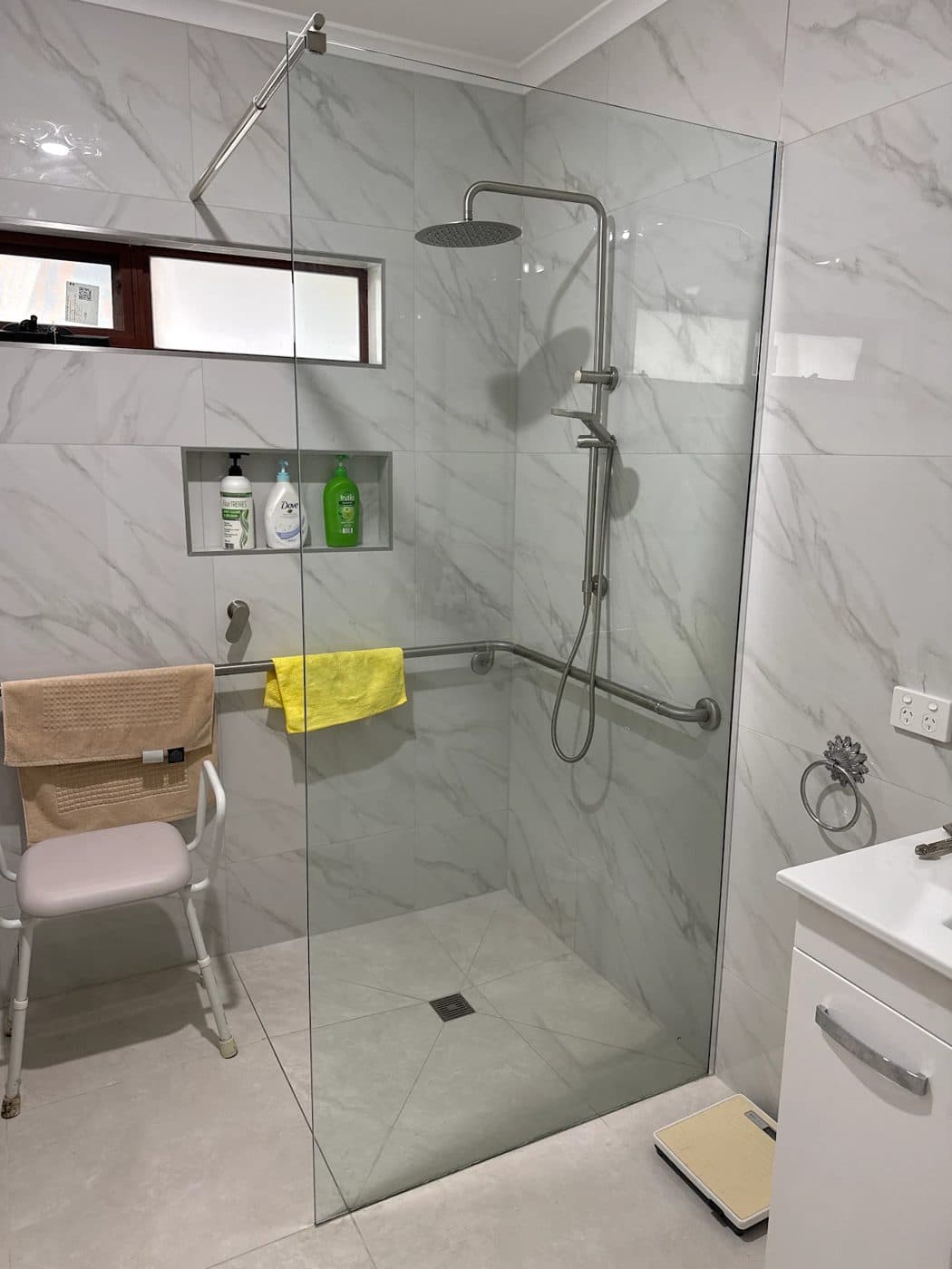 A frameless walk-in shower with a rain shower head, grab rails and a recessed shelf