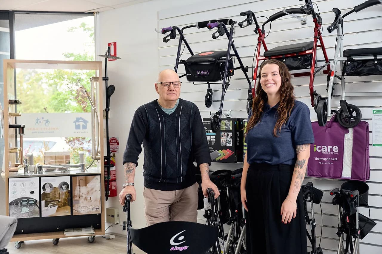 An older man trying a walker beside an Ability Ease team member, with walkers displayed on the showroom wall