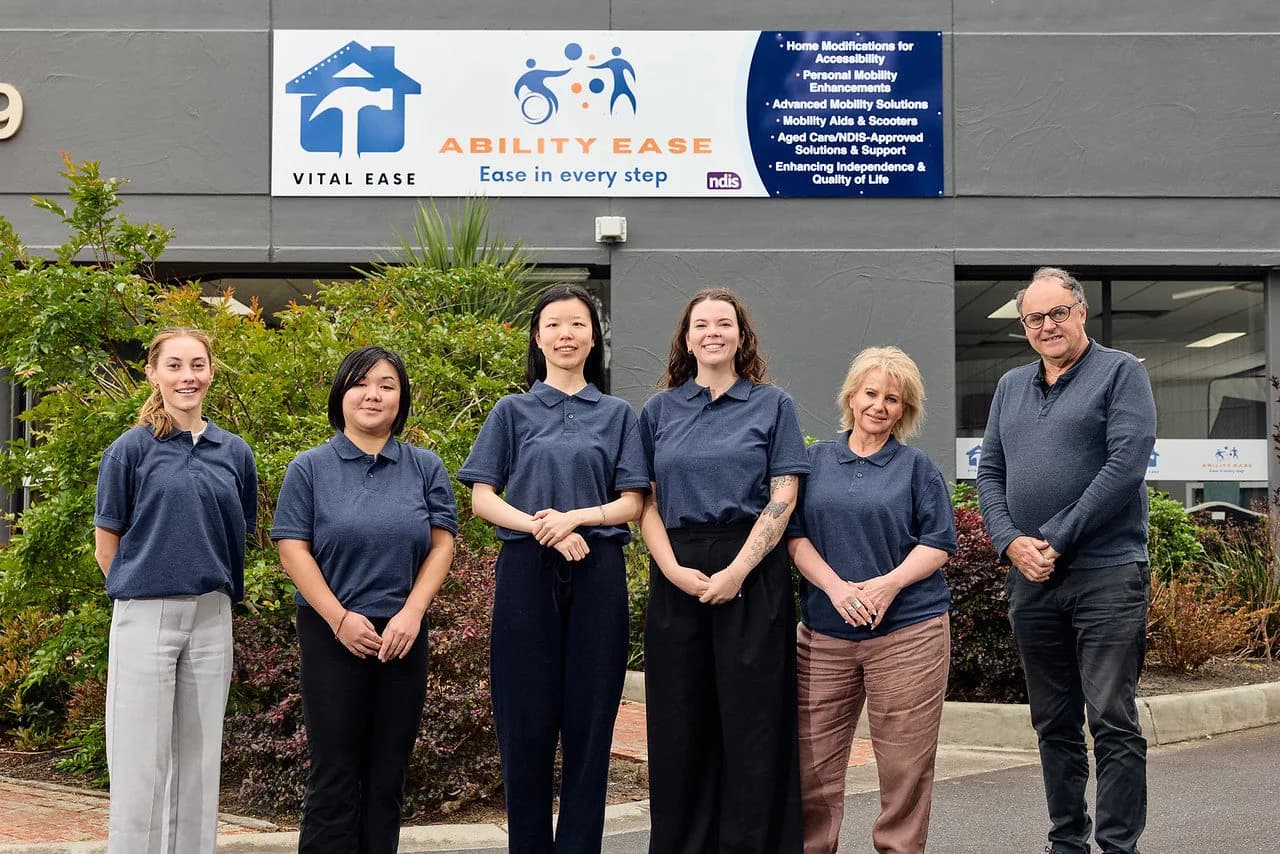 Six Ability Ease team members standing outside the showroom, under a sign showing the Vital Ease and Ability Ease logos