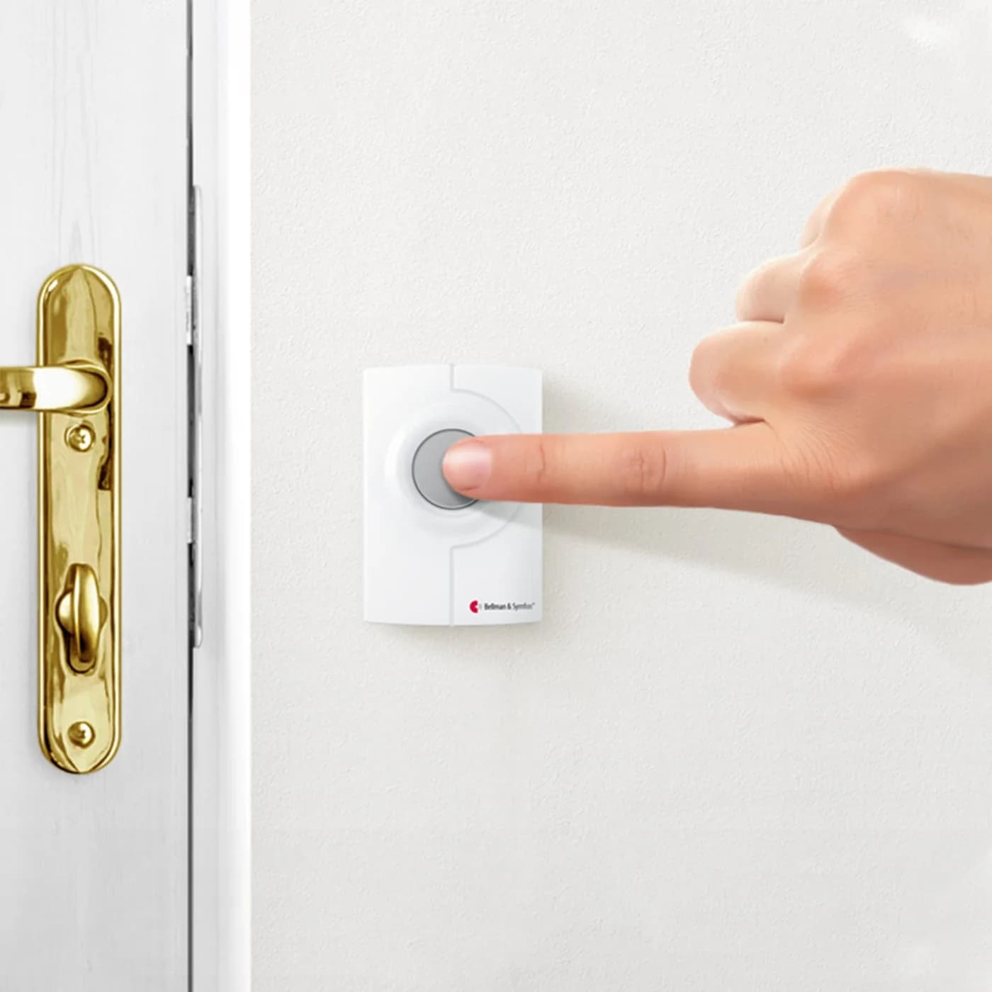 A finger pressing a white Bellman wireless doorbell push button mounted beside a front door handle