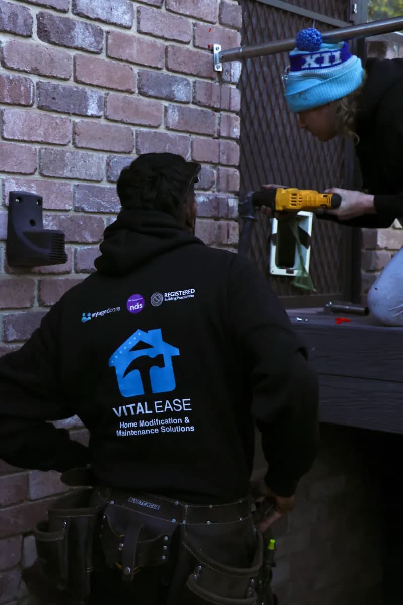 Two Vital Ease team members fixing a handrail bracket into a brick wall with a cordless drill