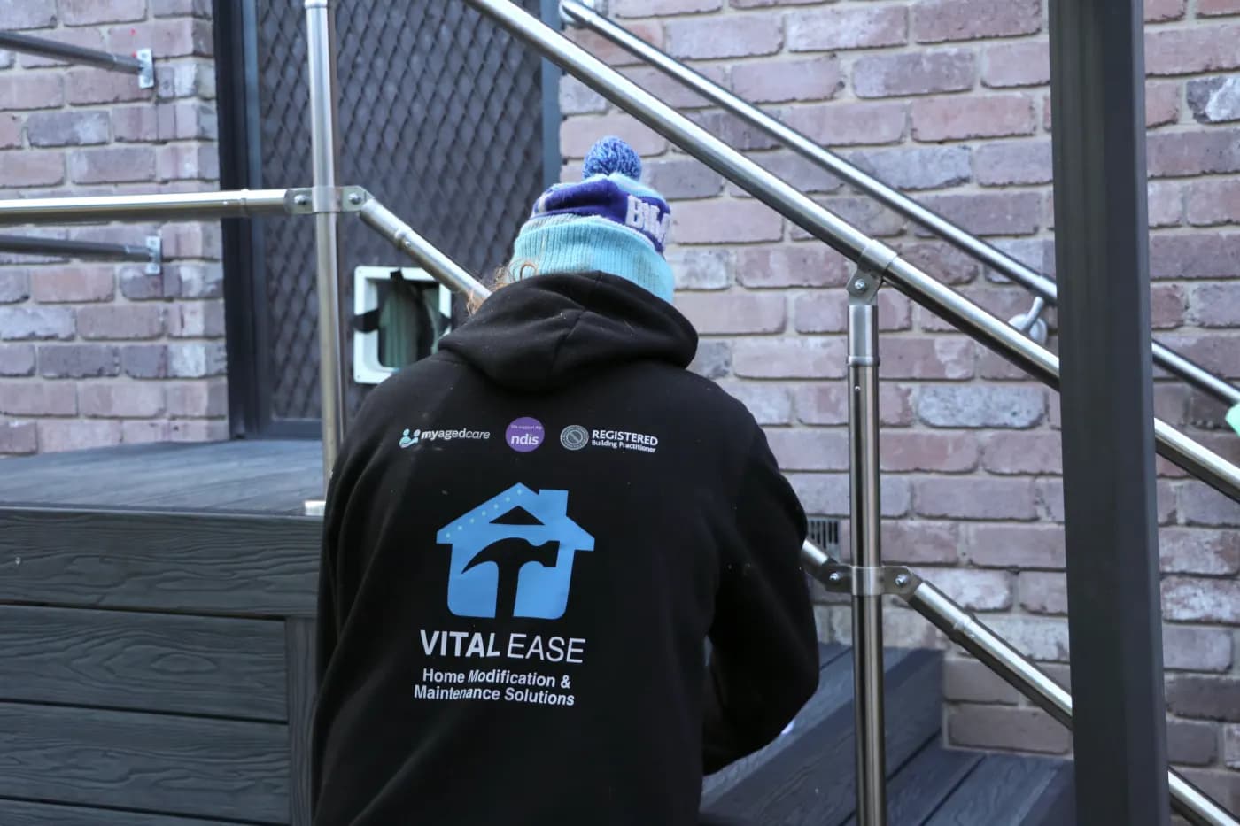 A Vital Ease tradesperson in branded uniform carrying My Aged Care, NDIS, and registered building practitioner accreditation marks