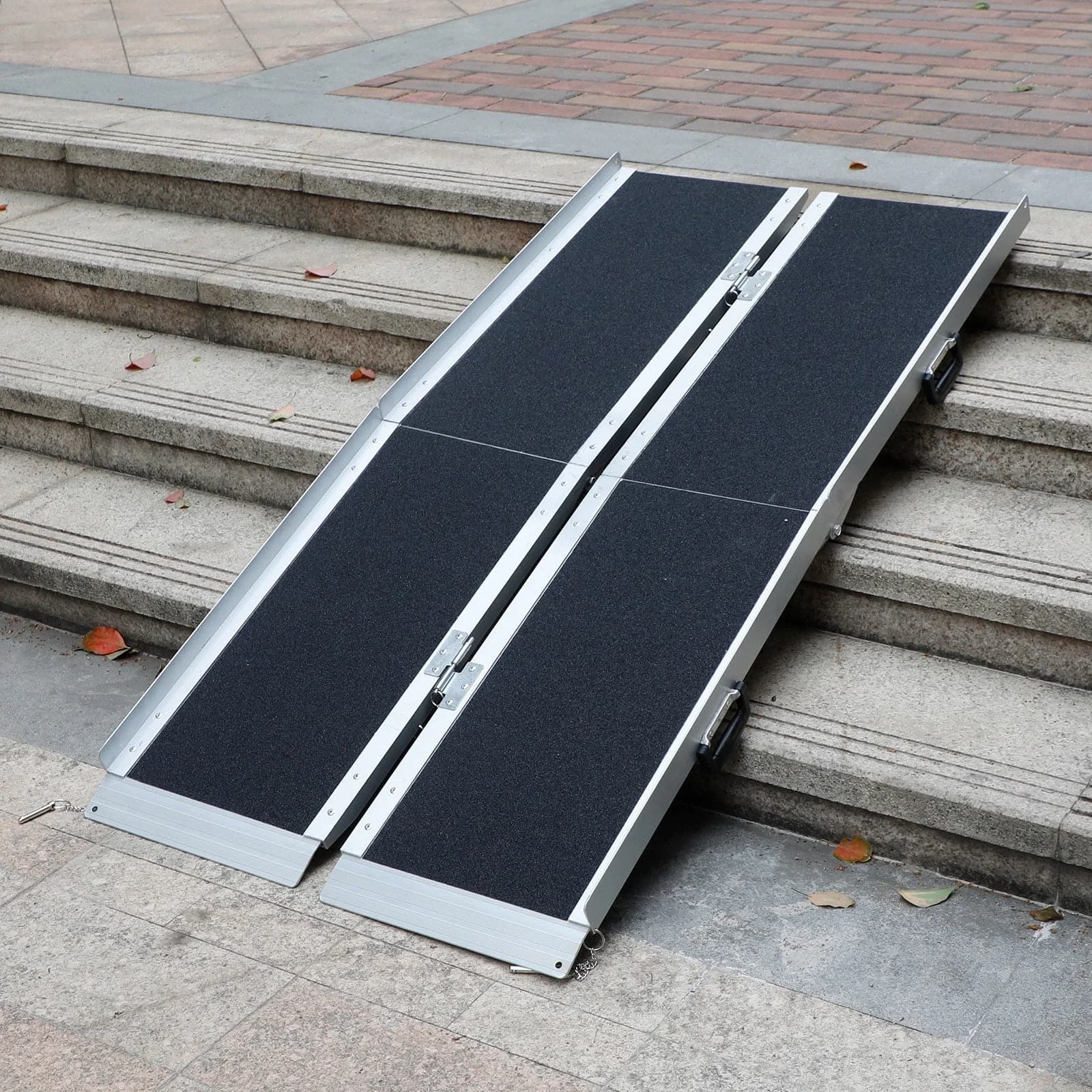 A folding aluminium suitcase ramp with a non-slip black surface, set up over a flight of concrete steps