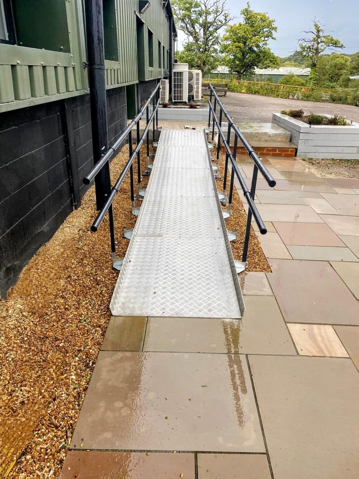 A long prefabricated metal ramp with handrails running beside a paved path to a building entrance