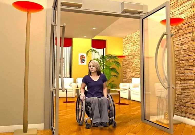 A woman in a wheelchair coming through a wide glass door into a brightly lit room