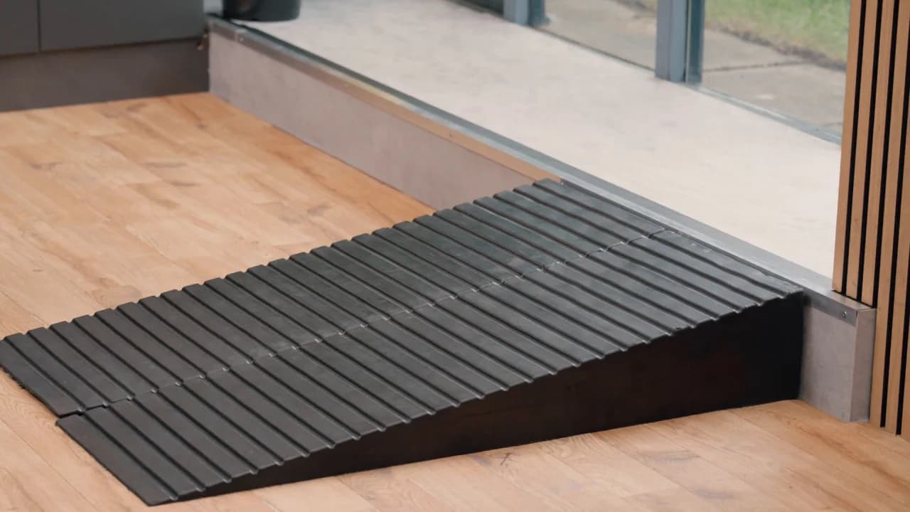 A black rubber threshold ramp laid against the track of a sliding door, meeting a timber floor