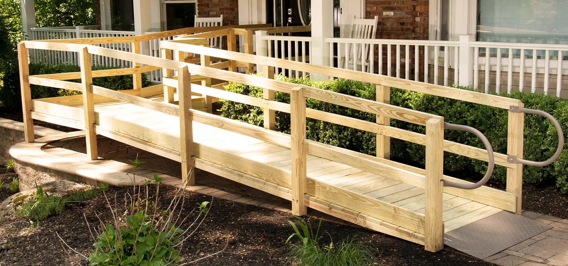 A custom-built timber wheelchair ramp with picket handrails on both sides, crossing a garden bed to a verandah