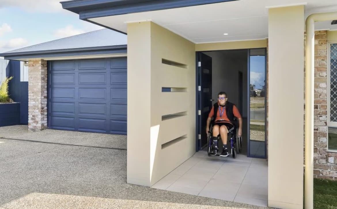 A person using a wheelchair at the level entrance of a modern Australian home, with a wide doorway and no step