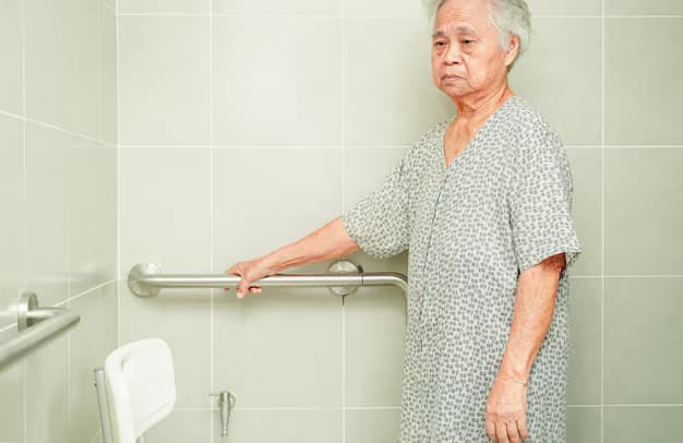An older woman at a green-tiled bathroom wall, holding a long horizontal grab rail beside a fold-down shower seat