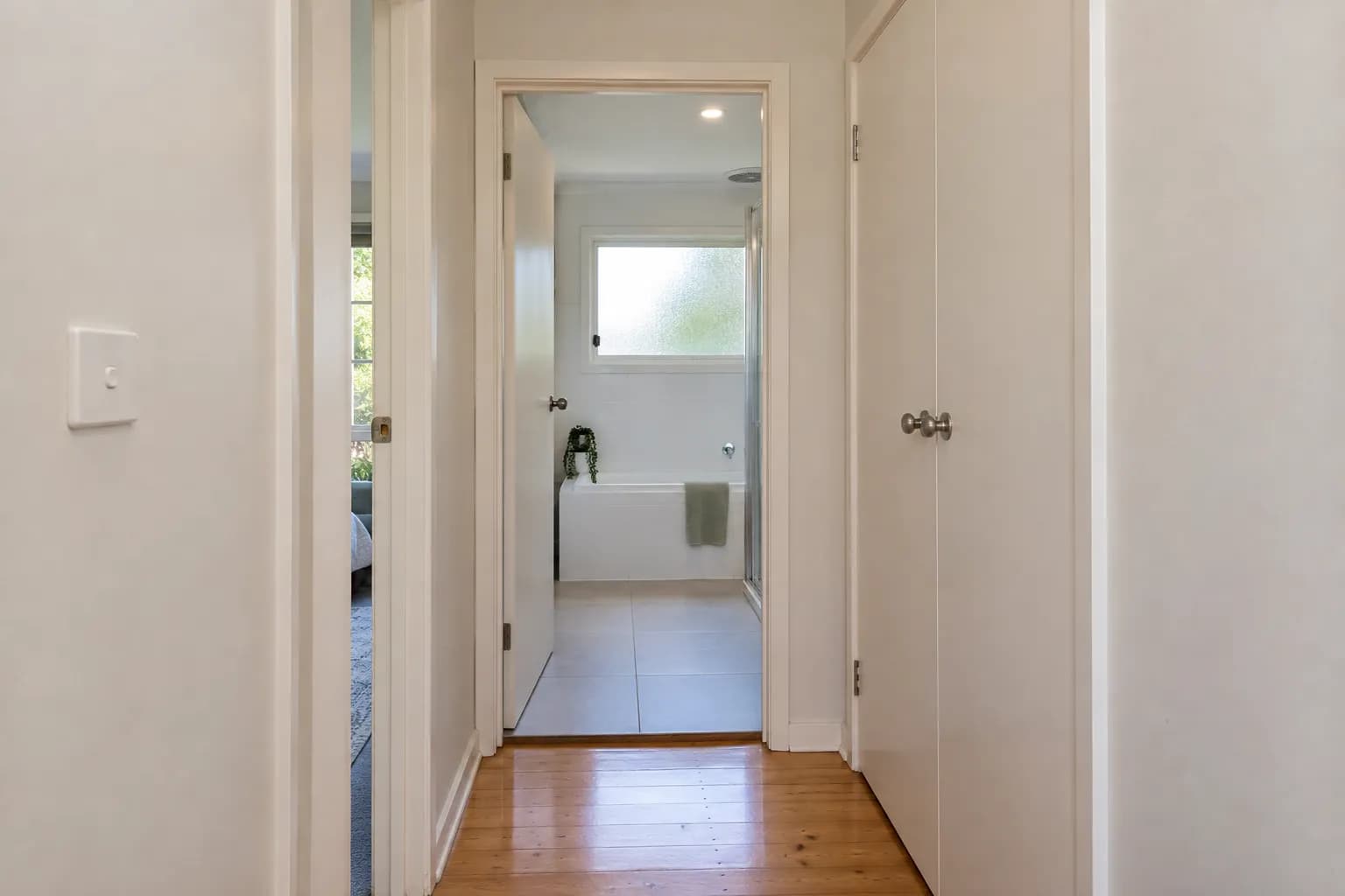 A narrow hallway with a bathroom door at the end and a cupboard door close beside it