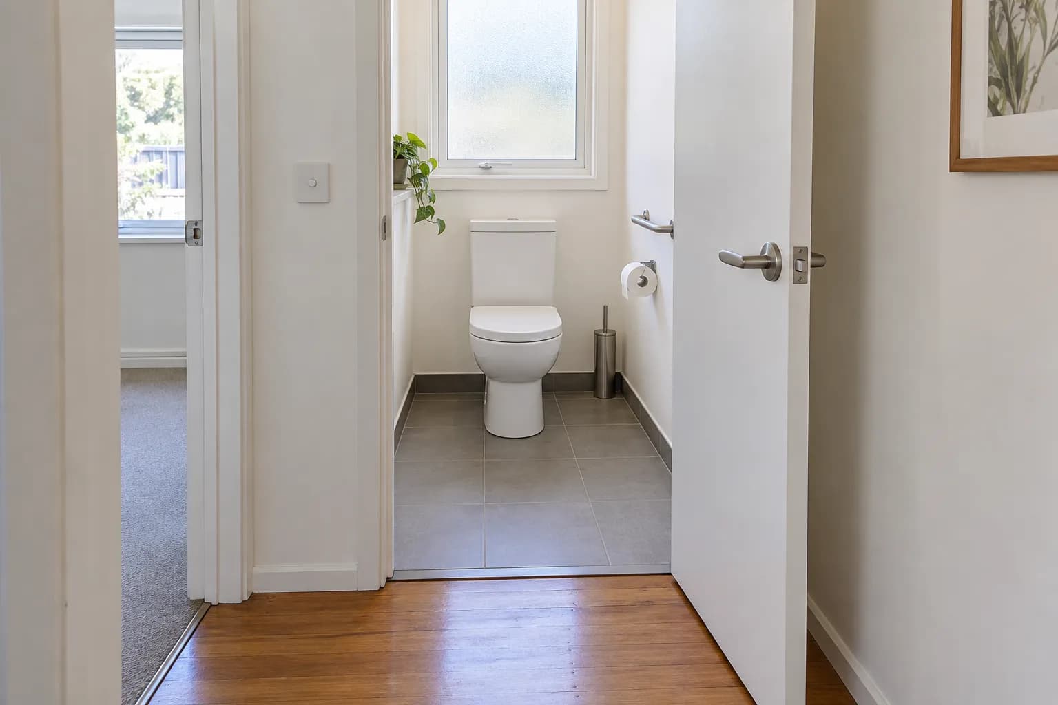 A separate toilet with a lever-handled door opening outwards, leaving the floor in front of the toilet clear