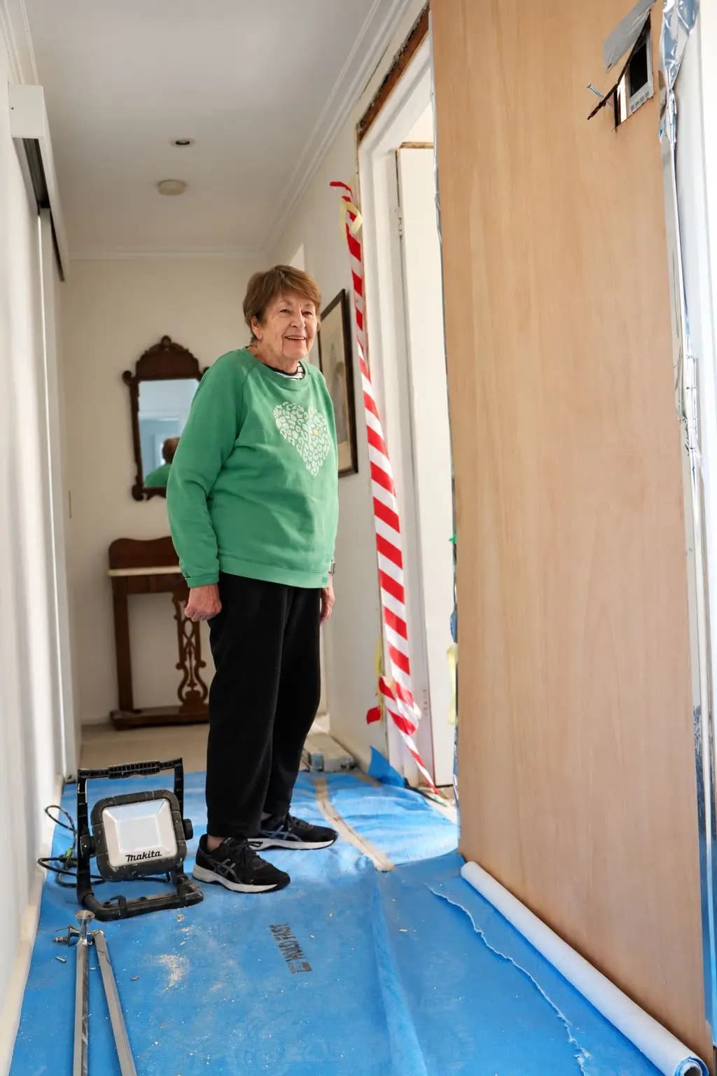 A smiling older woman in her hallway during doorway work, a new door leaning on the wall