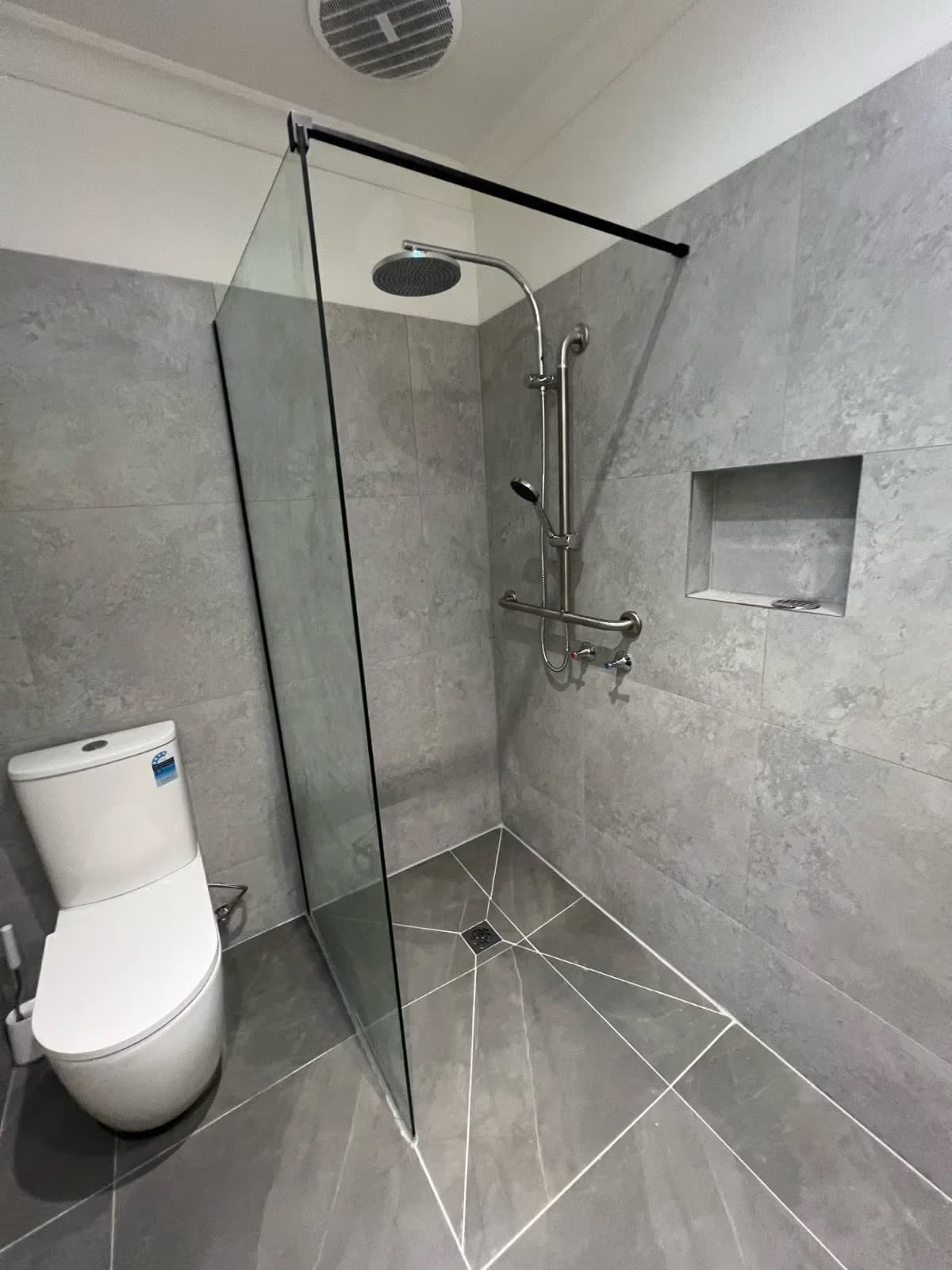 A grey tiled bathroom with a glass-screened shower and a basin, in a Melbourne home