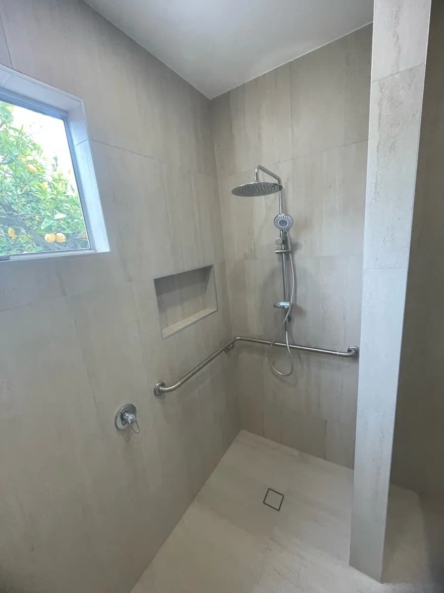 A tiled level-access shower with no step at the entry, a grab rail on the wall, and a recessed niche