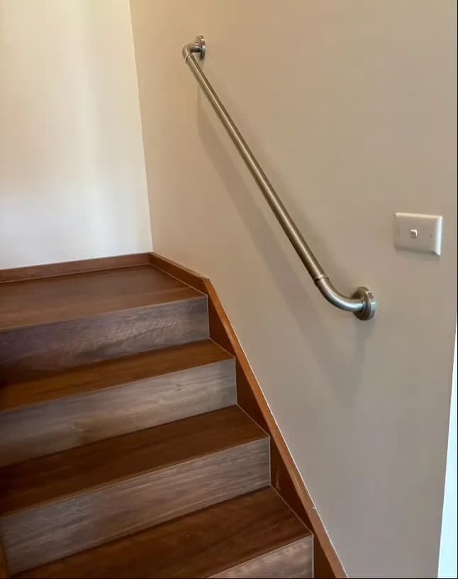 A stainless steel handrail mounted along the wall above a timber internal staircase