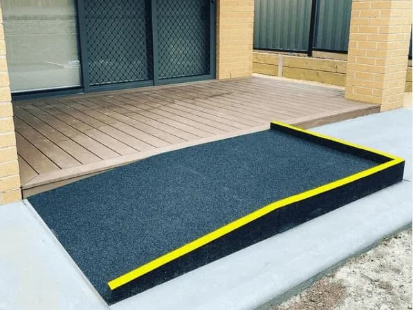 A black rubber threshold ramp with a yellow safety edge, set against a timber deck and concrete path