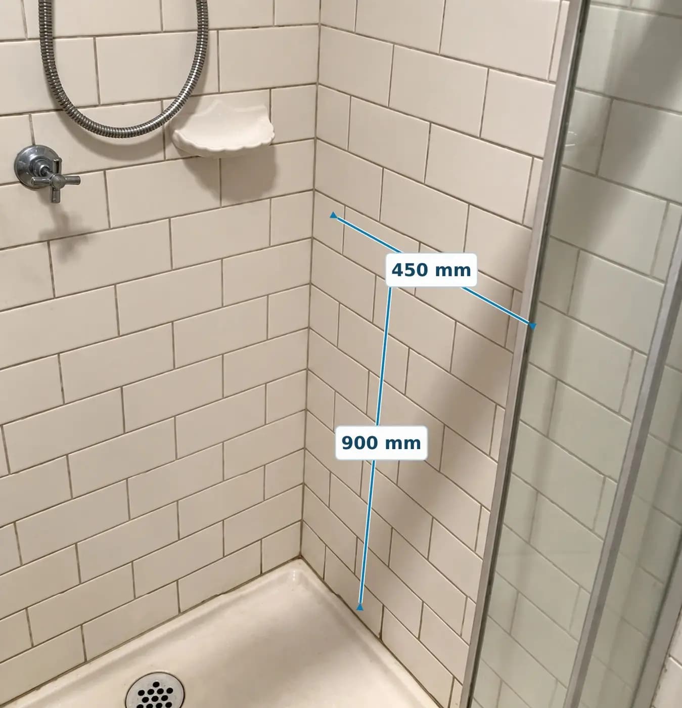 A tiled shower corner marked up for a grab rail, with lines showing 900 mm up from the shower base and 450 mm along the wall