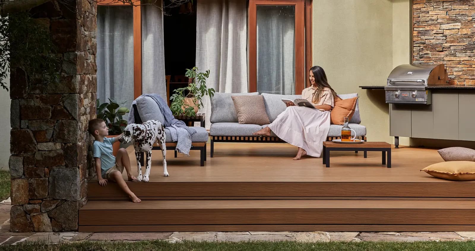 A woman and a child with a dalmatian on a wide composite deck with a low step down to the lawn