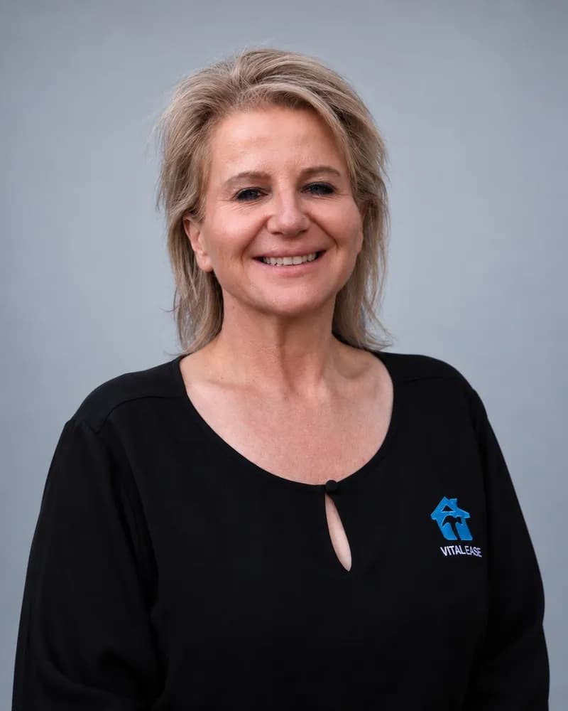 A smiling Vital Ease team member with shoulder-length blonde hair, in a black branded top